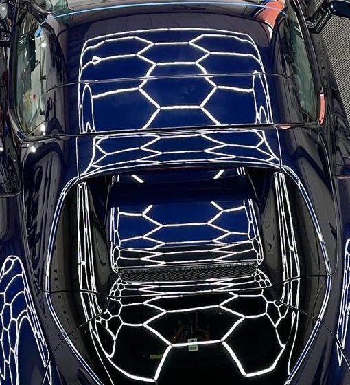 Detail van het lak: witte hexagonlijnen van de plafondverlichting spiegelen strak in de donkerblauwe carrosserie.