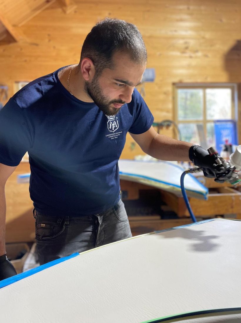 De eigenaar van MK Detailing werkt met een spuitpistool aan een wit paneel dat rondom is afgeplakt.